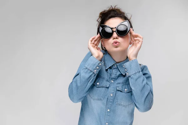 Junges brünettes Mädchen mit schwarzer Brille. Katzenbrille. Die Haare sind zu einem Dutt zusammengebunden. das Mädchen justiert seine Brille. — Stockfoto