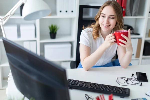 Mooi jong meisje werken met de computer in kantoor. Het meisje heeft een rode kop in haar handen. — Stockfoto