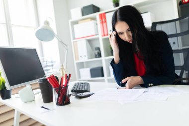 Güzel genç kız ofiste belgelerle masada çalışıyor ve bir kalem elinde tutuyor.