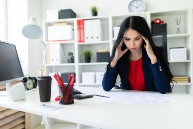 Güzel bir genç kız ofiste masada oturur ve onun ellerini başının tutar.