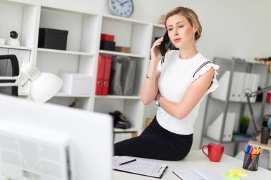 Genç sarışın kız ofiste masada oturan ve telefonda konuşurken.