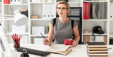 Ofisteki bir masada oturan genç bir kız elinde bir kalem ve kırmızı bir bardak tutuyor. Kız açık bir kitap gibi yalan söylemeden önce.
