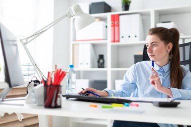 Ofiste genç bir kız bir masaya oturur, onun elinde bir kalem tutan ve bilgisayarda çalışır.