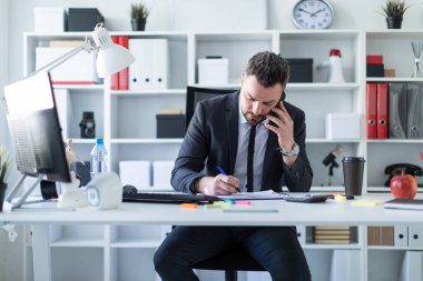 Bir adam masada, ofisinde oturuyor telefonda konuşurken ve belgeleriyle çalışma.