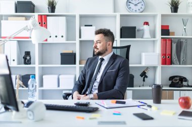 Bir adam masada ofiste bir sandalyede oturuyor.