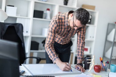 Bir adam ofiste masanın yanında duruyor ve bir işaretleyici manyetik tahtaya çizer.
