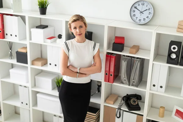 Genç sarışın kız Office belgeleri ile bir raf yanında duruyor.