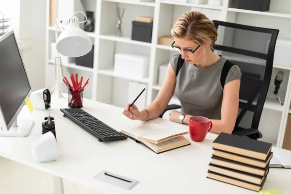 Een jong meisje is zittend aan een tafel in het kantoor, het bezit van een potlood in haar hand en lezen van een boek. — Stockfoto