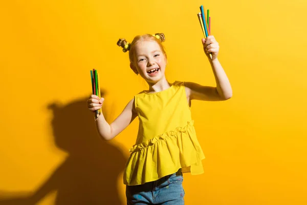 Ragazza con i capelli rossi su sfondo giallo. Una bella ragazza tiene in mano matite colorate . — Foto Stock