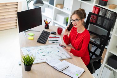 Genç bir kız bir banka kartı ve telefon elinde tutan ofiste, masada oturuyor.