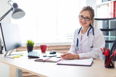 Beyaz bir elbise içinde genç bir kız bilgisayar masasında oturuyor.