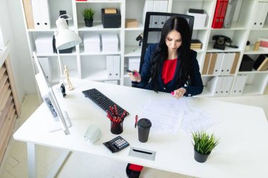 Güzel genç kız masa ofis belgeleri ile çalışıyor. Kız belgedeki önemli noktaları pembe bir marker ile vurgulamaktadır..