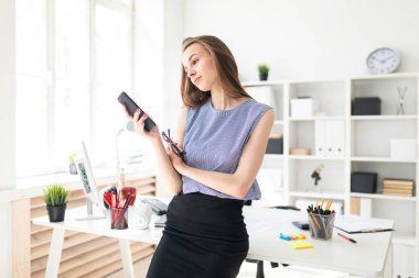 Güzel genç kız ofiste masanın ayakta, gözlük onun elinde tutan ve telefon ekrana bakarak.