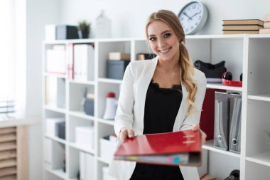 Genç bir kız ofis raf yanında duruyor ve belgeler ile kırmızı bir klasöre dışarı tutar.