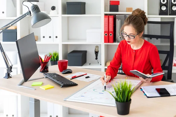 En ung flicka sitter vid ett bord på kontoret, innehar en markör i handen och arbetar med ett anteckningsblock och en magnetisk anslagstavla. — Stockfoto