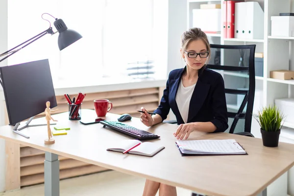 Een jong meisje is achter een computerbureau zit, houdt een potlood in haar hand en werken met documenten. — Stockfoto