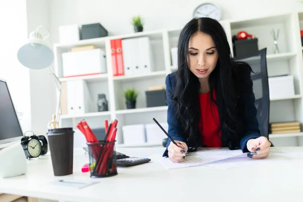 Beautiful young girl is working with documents in the office at the table and is holding a pencil in her hand. — Stock Photo, Image