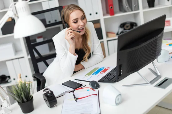 Seorang gadis muda dengan headphone dengan mikrofon duduk di meja di kantor dan melihat ke monitor . — Stok Foto