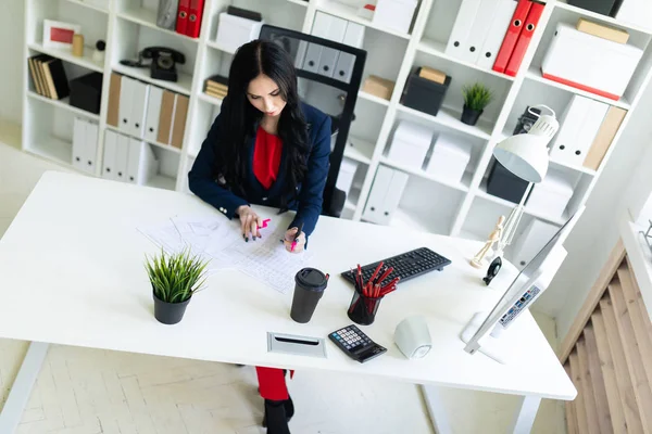 Güzel genç kız masa ofis belgeleri ile çalışıyor. Kız belgedeki önemli noktaları pembe bir marker ile vurgulamaktadır..