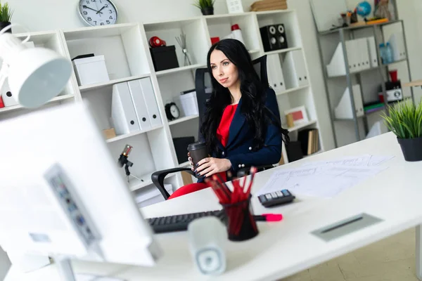 Güzel bir genç kız bir bardak kahve tablo ofiste bir sandalyede oturup ile düzenliyor.