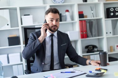 Bir adam ofiste masa başında oturan, telefonda konuşurken ve bir bardak kahve holding.