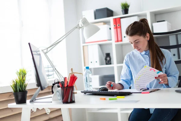 Genç bir kız ofiste bir masada oturur ve çıkartmalar belgelerdeki tutkallar.