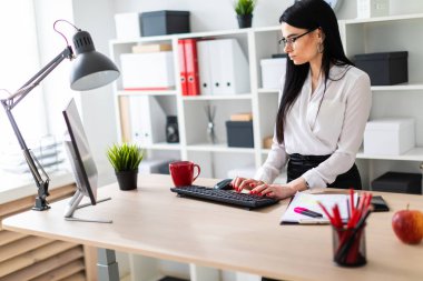 Genç bir kız masanın ayakta ve metin klavyede yazarak. Belgeler ve bir işaretleyici kızın yanında yalan.