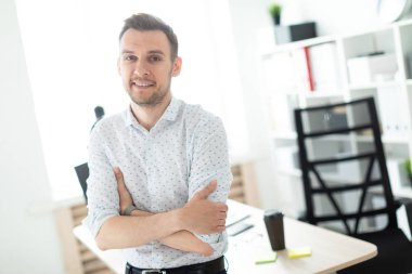 Genç bir adam ofiste bir masaya yaslanmış duruyor..