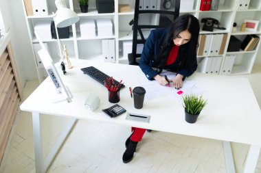 Güzel genç kız masa ofis belgeleri ile çalışıyor. Kız belgedeki önemli noktaları pembe bir marker ile vurgulamaktadır..