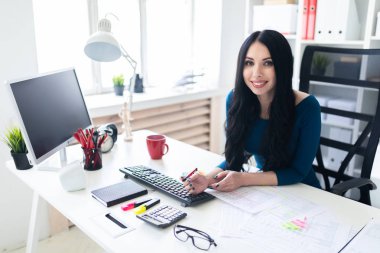 Genç bir kız masada ofiste oturur, onun elinde bir kalem tutan ve belgeleri doldurur.