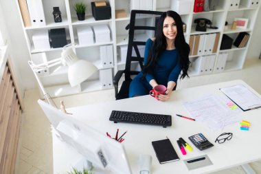 Genç bir kız ofiste masada oturur ve kırmızı bir fincan elinde tutan.