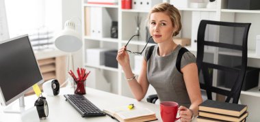 Genç bir kız ofiste bir masada oturuyor ve elinde kırmızı bir bardak ve gözlük tutuyor. Kız açık bir kitap gibi yalan söylemeden önce.