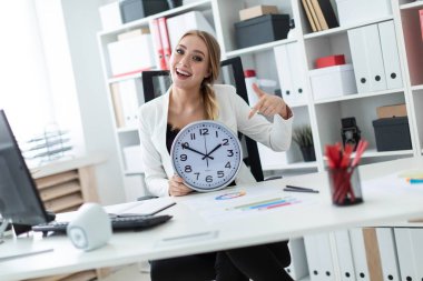 Genç bir kız ofiste bir masada oturur ve saat yüzünü puan bir parmak.