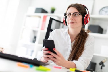 Genç bir kız kulaklık ofiste bir masada oturur ve bir telefon elinde tutan.