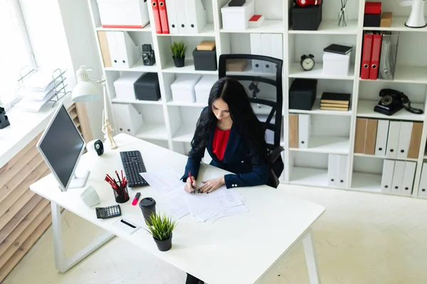 Güzel genç kız masada ofiste oturan belgeleri doldurur.