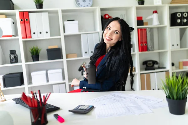 Güzel bir genç kız bir bardak kahve tablo ofiste bir sandalyede oturup ile düzenliyor.