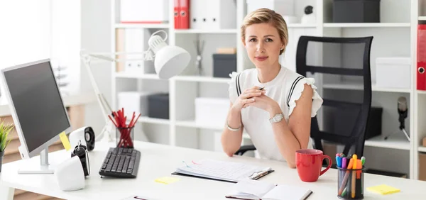 Een jong blond meisje zit achter een computerbureau in het kantoor en een potlood in haar hand houdt. — Stockfoto