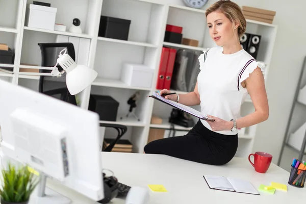 Una joven rubia está sentada en el escritorio de la oficina y tiene documentos y un lápiz.. — Foto de Stock