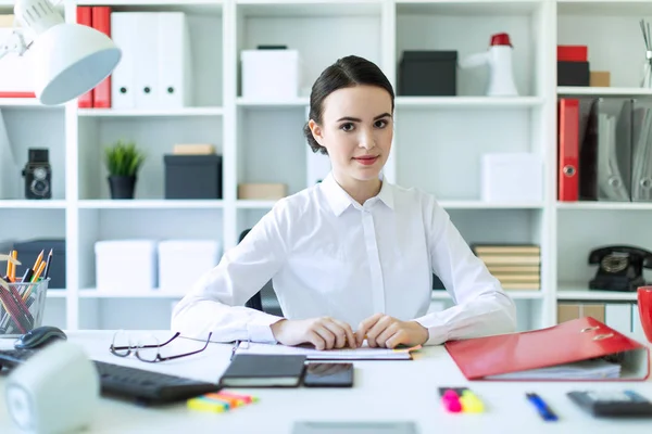 En ung flicka på kontoret sitter vid ett bord och håller en penna i händerna. — Stockfoto