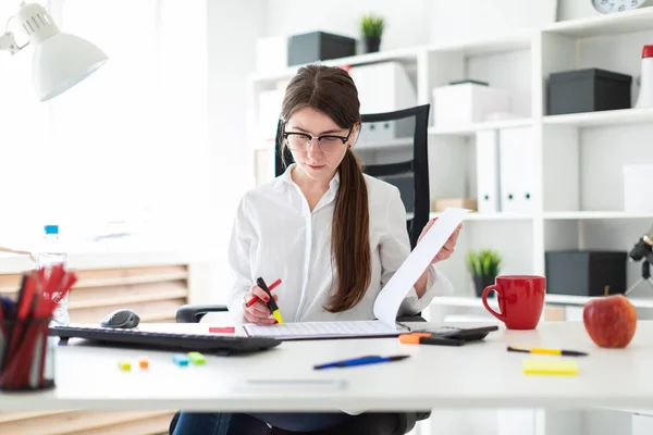 En ung flicka sitter vid ett bord på kontoret, hålla en penna i handen, en markör och arbeta med dokument. — Stockfoto