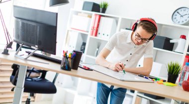 Gözlüklü ve kulaklıklı genç bir adam manyetik tahtaya bir işaret çizer..