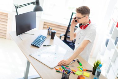 Gözlüklü genç bir adam bir bilgisayar masası duruyor ve telefonda konuşuyor. Önce onu bir manyetik kurulu ve işaretleri yatıyor. Çocuklar kulaklık boynuna asmak.