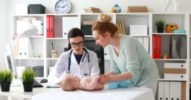 O masanın üzerinde yatan çocuk inceleyerek doktor ile anne 