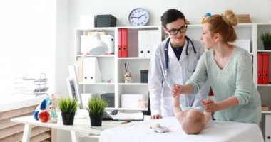 Doktor ile randevu sırasında masanın üzerinde yatan bebek el jimnastik yaparken anne