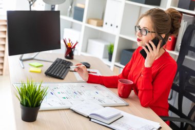 Genç bir kız ofiste masasında oturmuş, elinde kalem tutan ve telefonda konuşurken. Bir defter ve bir manyetik kurulu önünde kız yalan.