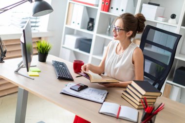 Genç bir kız bir bilgisayar masada oturur ve açık bir kitap onun elinde tutan ve ekrana görünüyor.