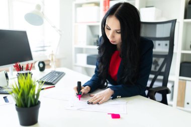 Güzel genç kız masa ofis belgeleri ile çalışıyor. Kız belgedeki önemli noktaları pembe bir marker ile vurgulamaktadır..