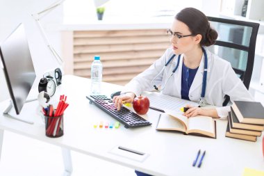 Beyaz bir elbise içinde güzel bir genç kız bir masaya oturur, onun elinde tutan bir işaretleyici ve bir kalem ve bir bilgisayar ve belgeler ile çalışır.