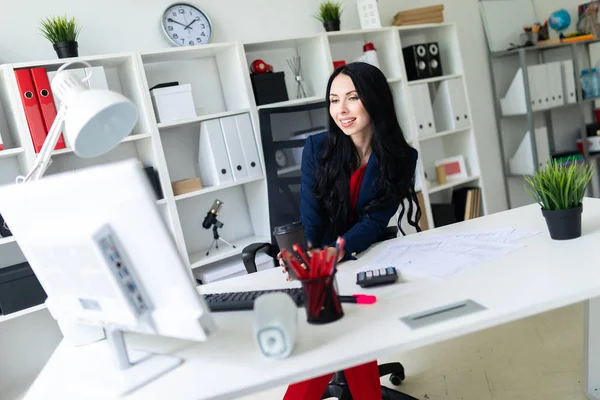 Bir bardak kahve ile tutarak ve tablo ofiste bir sandalyede oturan monitör bakarak güzel genç kız.