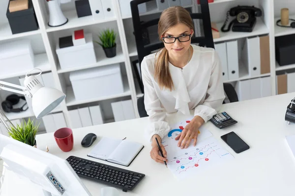 Een jong meisje aan een computerbureau op kantoor zit en een potlood in haar hand houdt. — Stockfoto